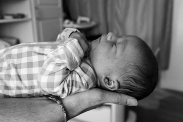 Black and white photo of a newborn baby resting peacefully in an adult's hand.