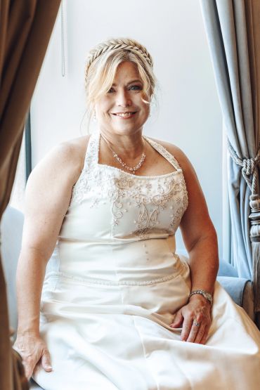 Woman in bridal gown sitting by the window.