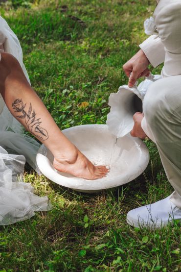 Person washing another's foot outdoors on grass.