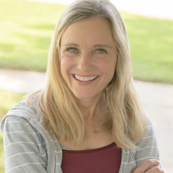 Smiling woman with blonde hair wearing a gray striped hoodie and maroon top.