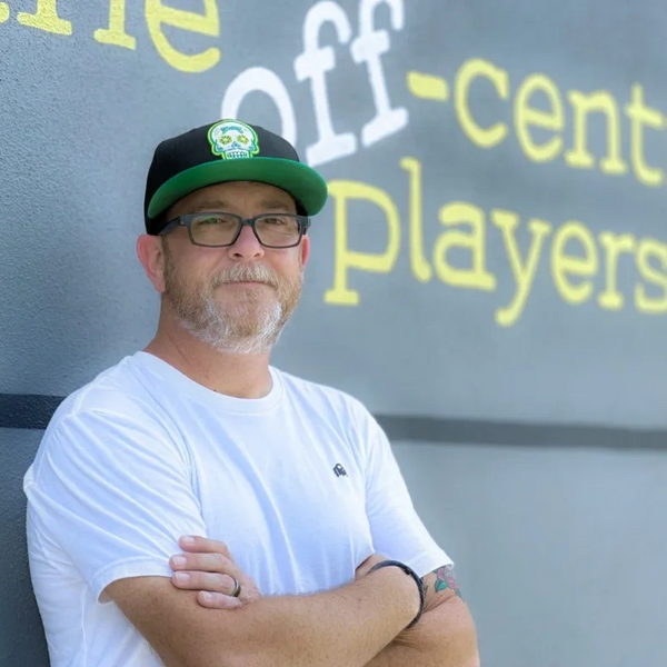 Man with glasses and cap standing confidently with arms crossed.