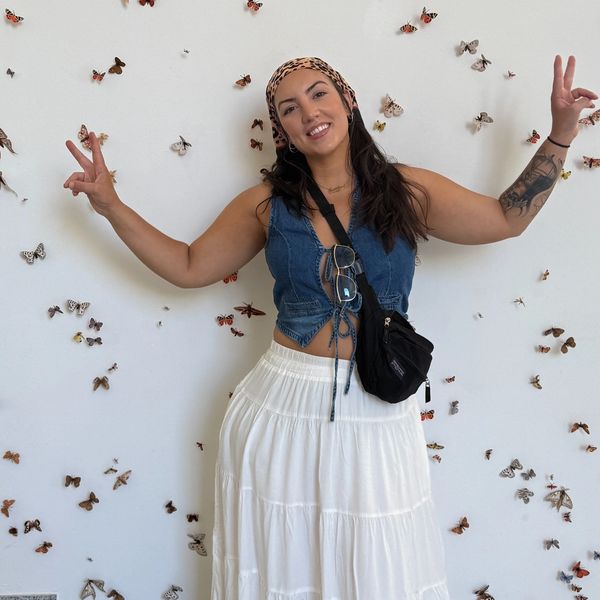A smiling woman poses with peace signs against a butterfly-decorated wall.