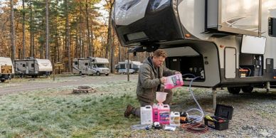 Man preparing RV antifreeze and maintenance supplies outdoors.
