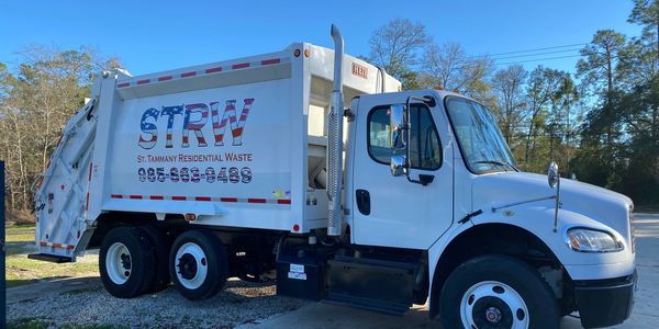 White garbage truck for St. Tammany Residential Waste parked outdoors.