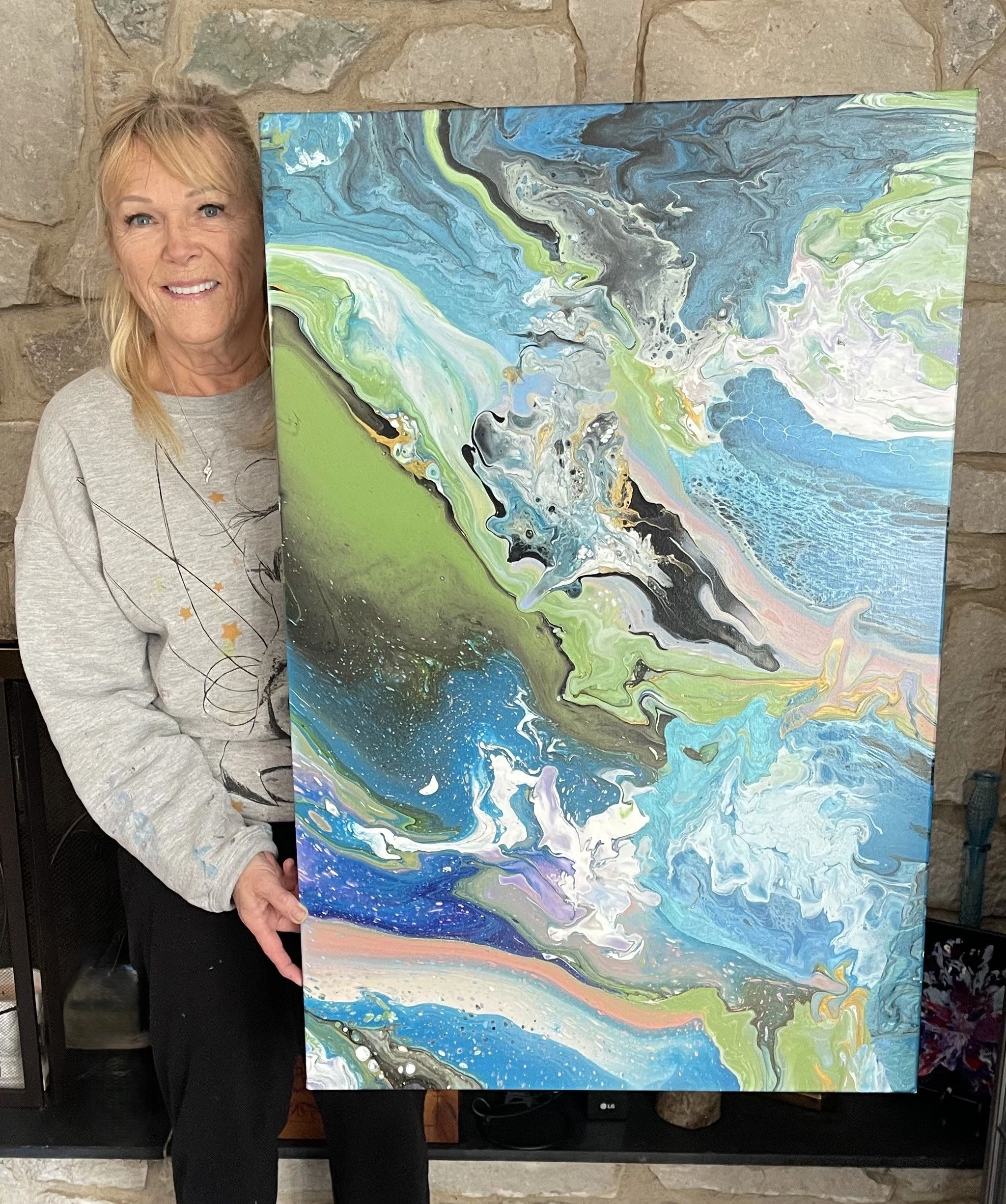 A woman proudly holds a colorful abstract painting with swirling blues, greens, and whites.