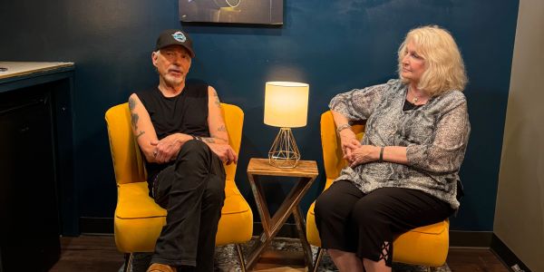 Two people seated in yellow chairs with a lamp between them.
