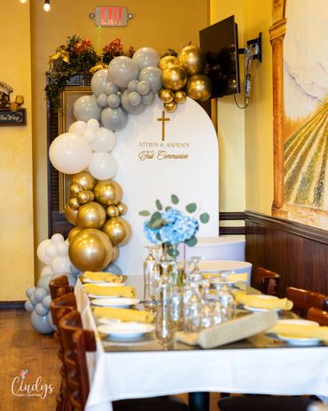 Elegant first communion celebration table with gold, silver, and white balloon decor.