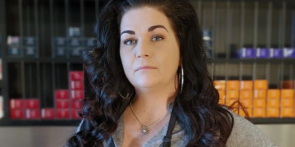 Confident woman with dark hair stands in front of shelves with colorful boxes.