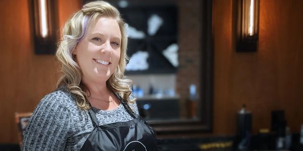 Smiling woman in a salon apron with stylish blonde hair.