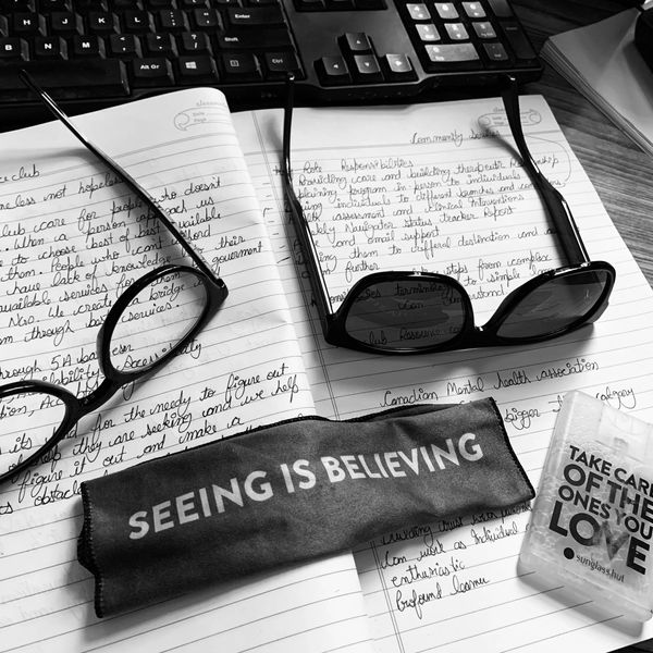 Black and white image of Gucci glasses on handwritten notes with a cloth that says 'SEEING IS BELIEVING'.