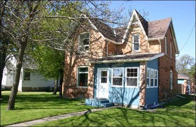 A brick house with a blue porch and green lawn.