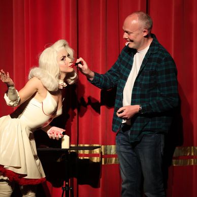 A man applies makeup on a performer dressed as Marilyn Monroe on stage.
