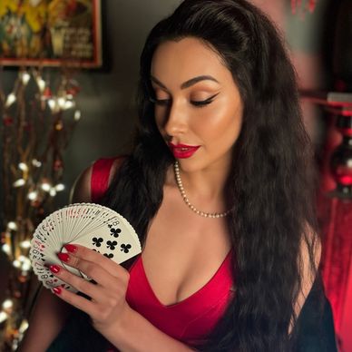 Woman in red dress holding a fan of playing cards, looking down.