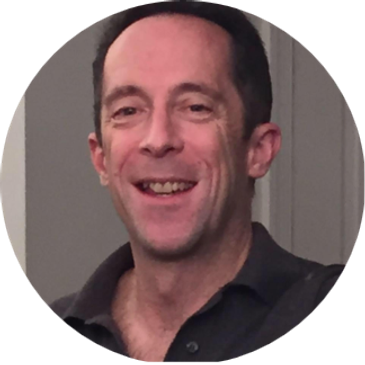 Smiling man in a dark shirt against a neutral background.