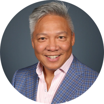 Smiling man in a blue checkered blazer and pink shirt against a gray background.