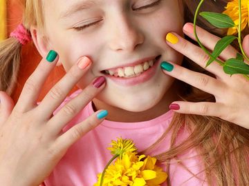 Little girl smiling, showing hands with colorful nail polish.