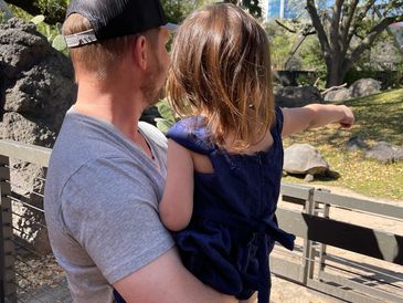 Photo of father and infant daughter. The daughter is pointing at an animal off scene.