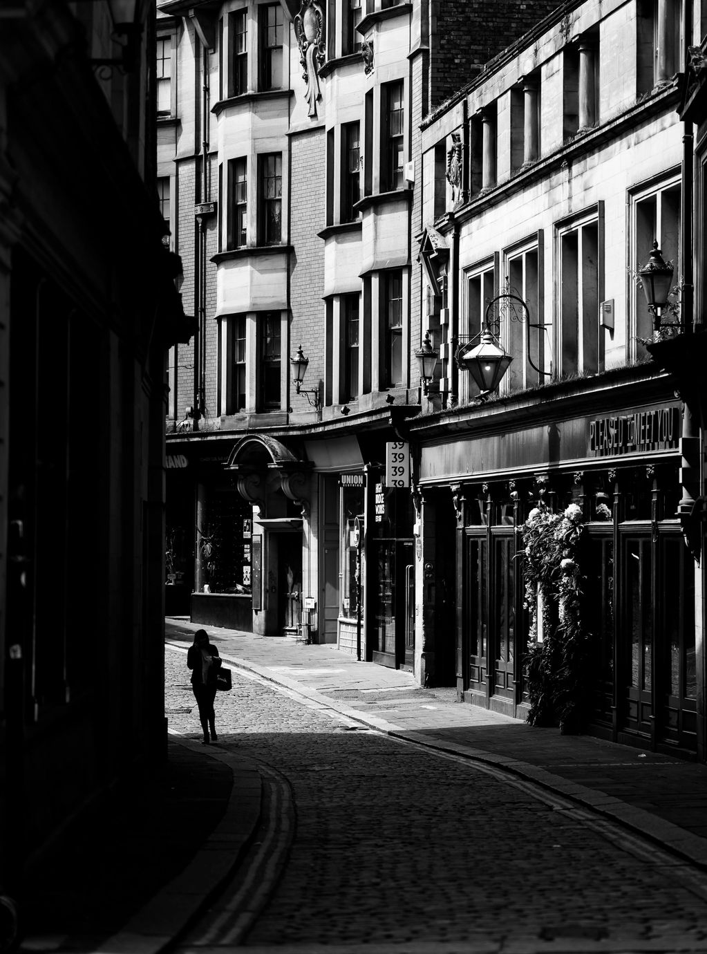 Vertical Black and White picture of Newcastle side street show storefronts and woman walking. 