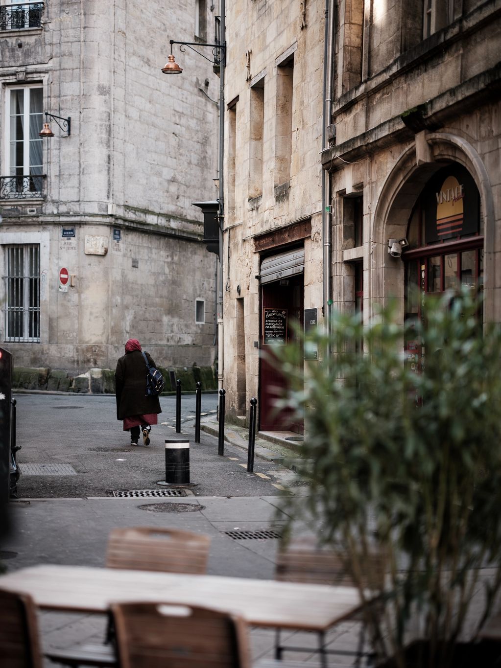 Vertical colour photograph of a women walking away from the camera along a side street in Bordeaux. 