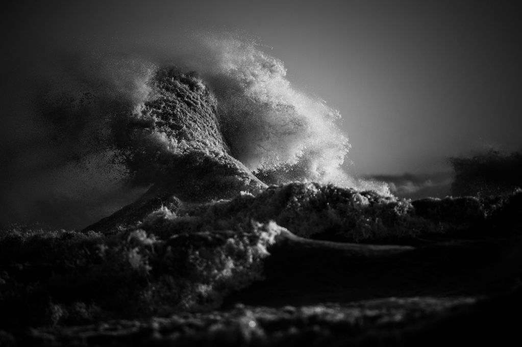 Dramatic Black and white landscape image showing a wave exploding into the sky during a storm.  