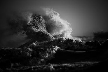 Dramatic Black and white landscape image showing a wave exploding into the sky during a storm.  