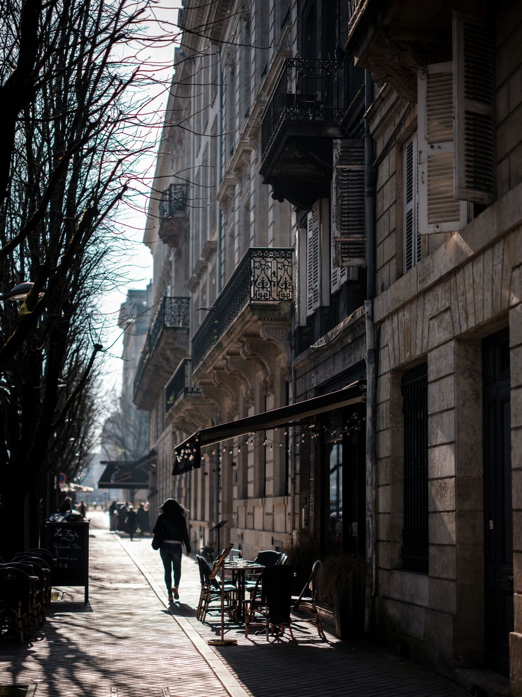 Colour vertical image, taken in early morning, showing a woman walking on a sidewalk in Bordeaux. 