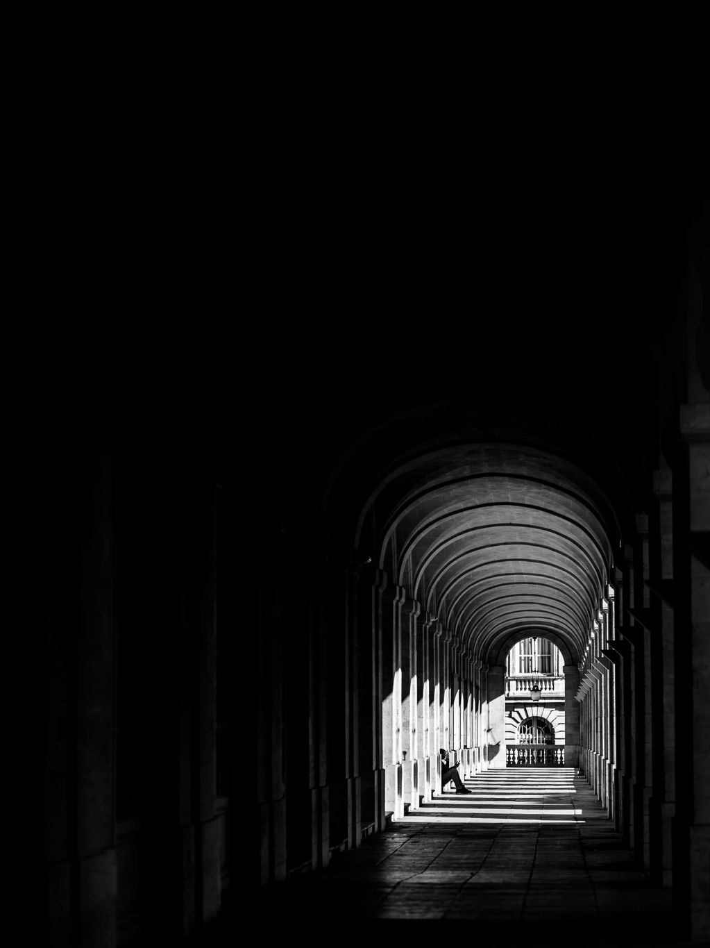 Black and White vertical image showing a person sitting alone in Bordeaux, France. 