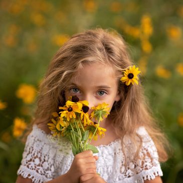 Young girl holding bright yellow flowers close to her face outdoors.