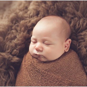 Sleeping newborn wrapped in a brown blanket on a soft textured surface.