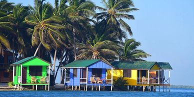Colorful cabins in tropical waters with palm trees and a clear blue sky.