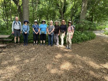 A group of eight people standing together in a wooded park area.