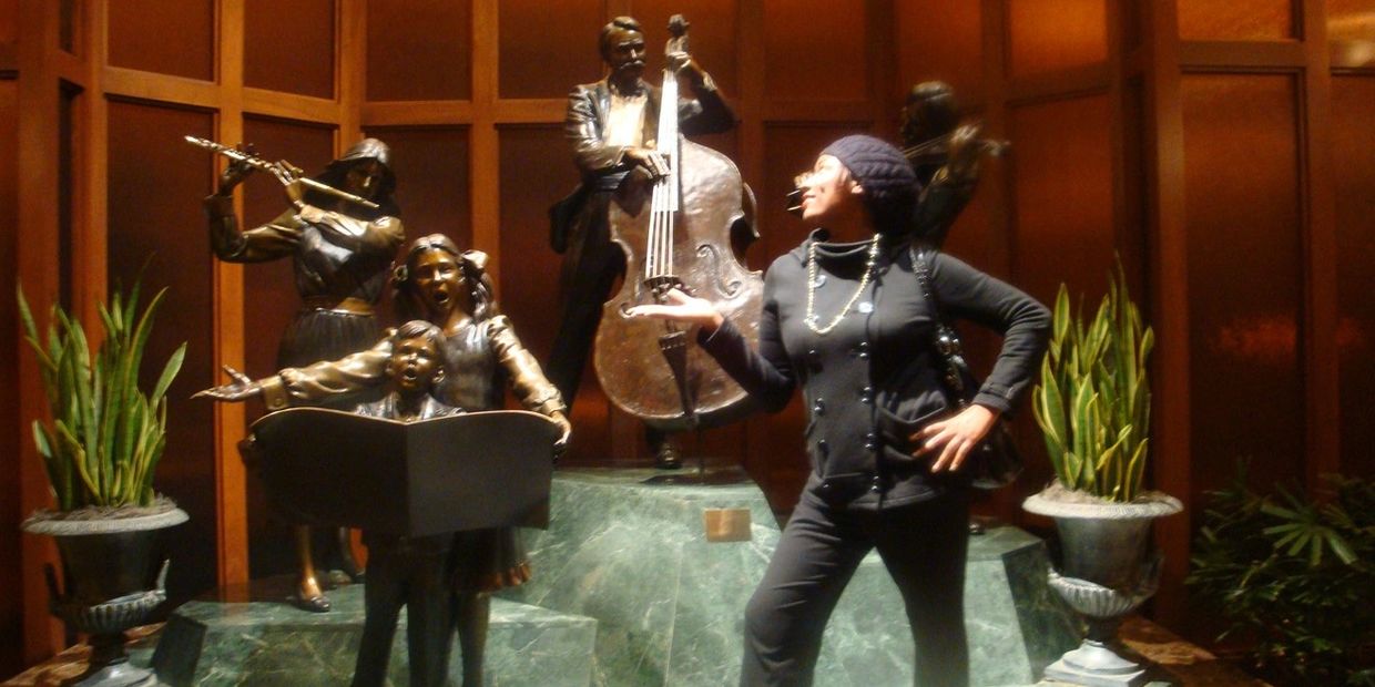 Woman posing with bronze musical statues in an indoor setting.