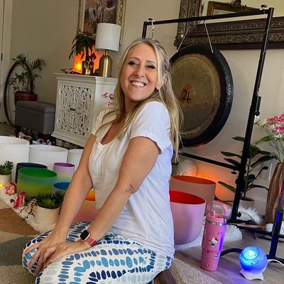Smiling woman sitting in a serene room with colorful singing bowls and a gong.