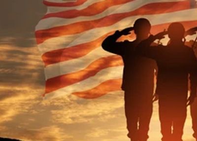 Silhouetted soldiers salute an American flag at sunset.