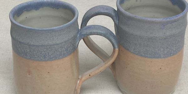 Two ceramic mugs with blue and beige glaze, placed side by side.