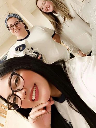 Four smiling women posing for a cheerful group selfie indoors.