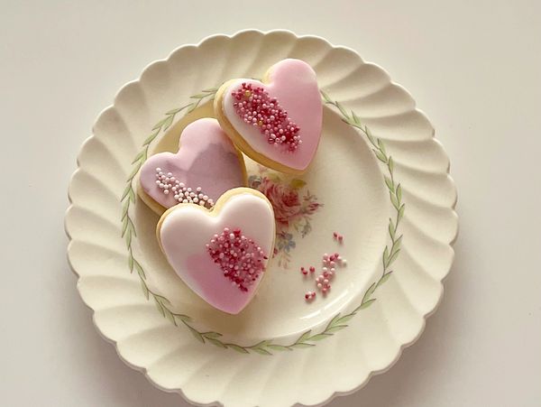 Three heart-shaped cookies with pink icing and sprinkles on a floral plate.