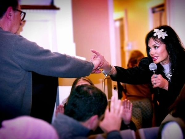 A woman holding a microphone reaches out to shake a man's hand.