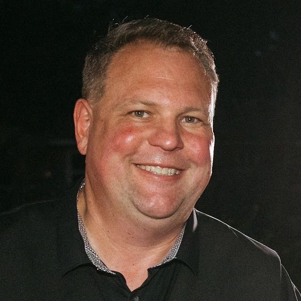Smiling man in a black shirt against a dark background.