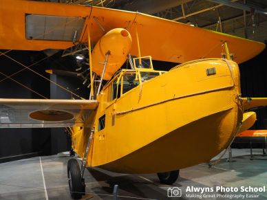 Bright yellow vintage seaplane displayed indoors in a museum.