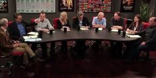 A group of eight people seated around a large oval table in discussion.