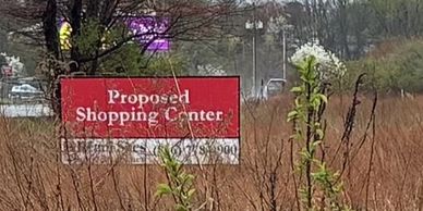 Sign for a proposed shopping center in a field.