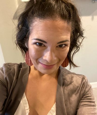 Woman smiling with large earrings and brown jacket.