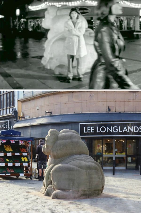 A person stands near a lion sculpture at night, while another walks by.