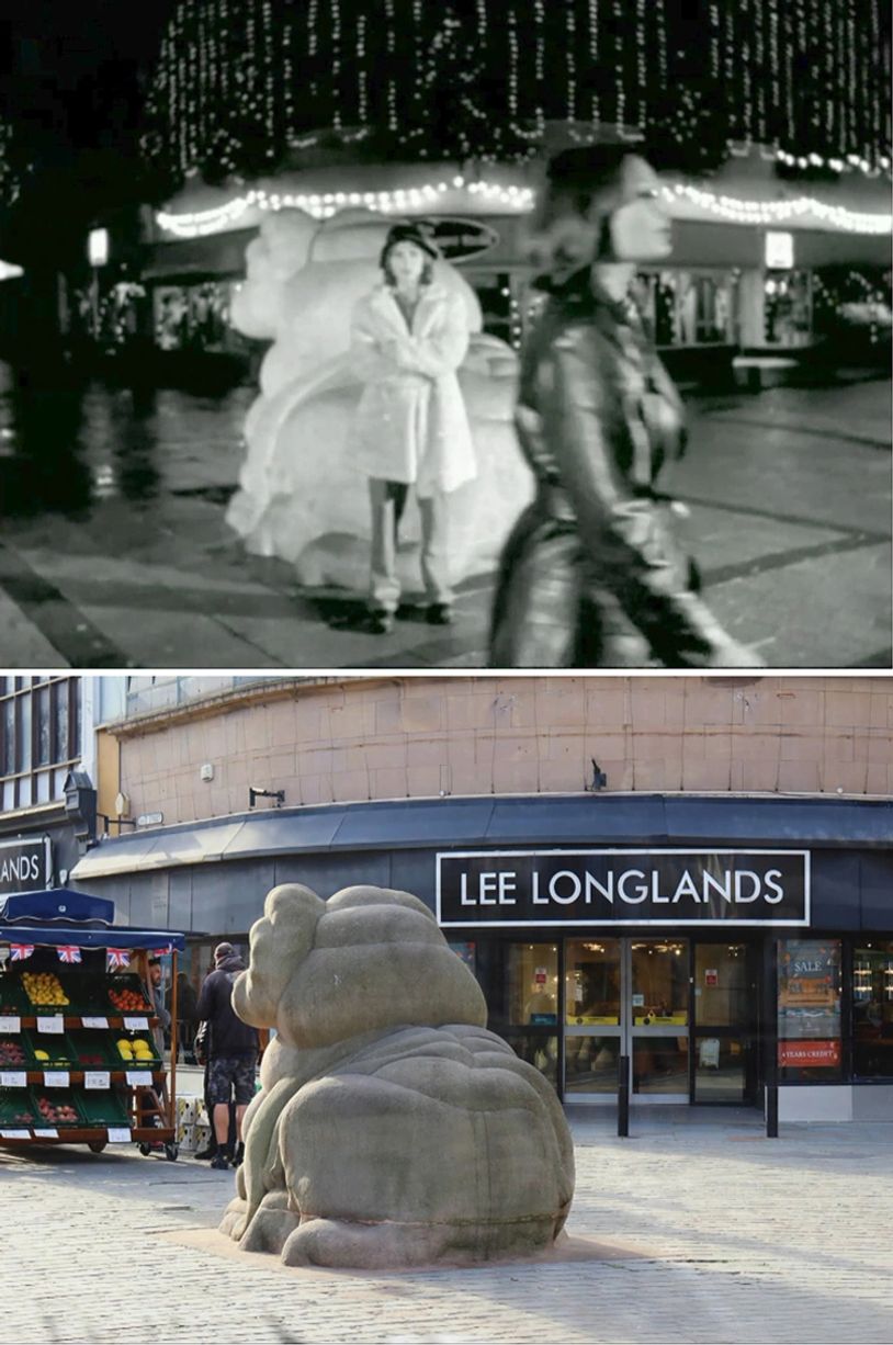 A person stands near a lion sculpture at night, while another walks by.