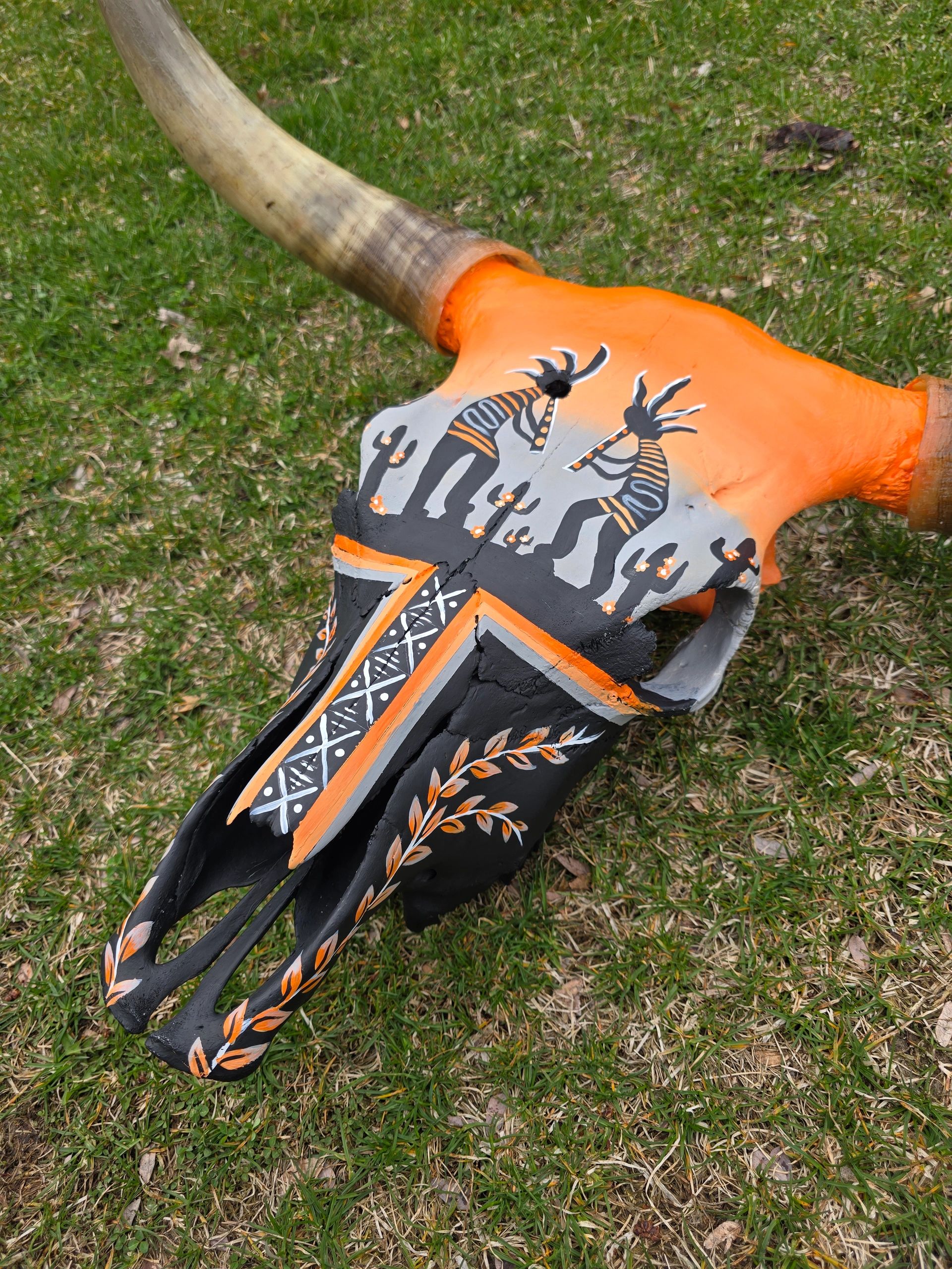 Painted animal skull with tribal art on grass.
