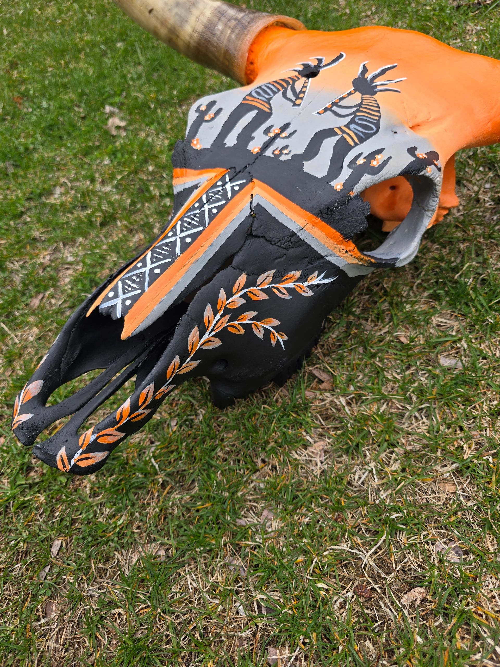 Painted animal skull with tribal designs on grass.