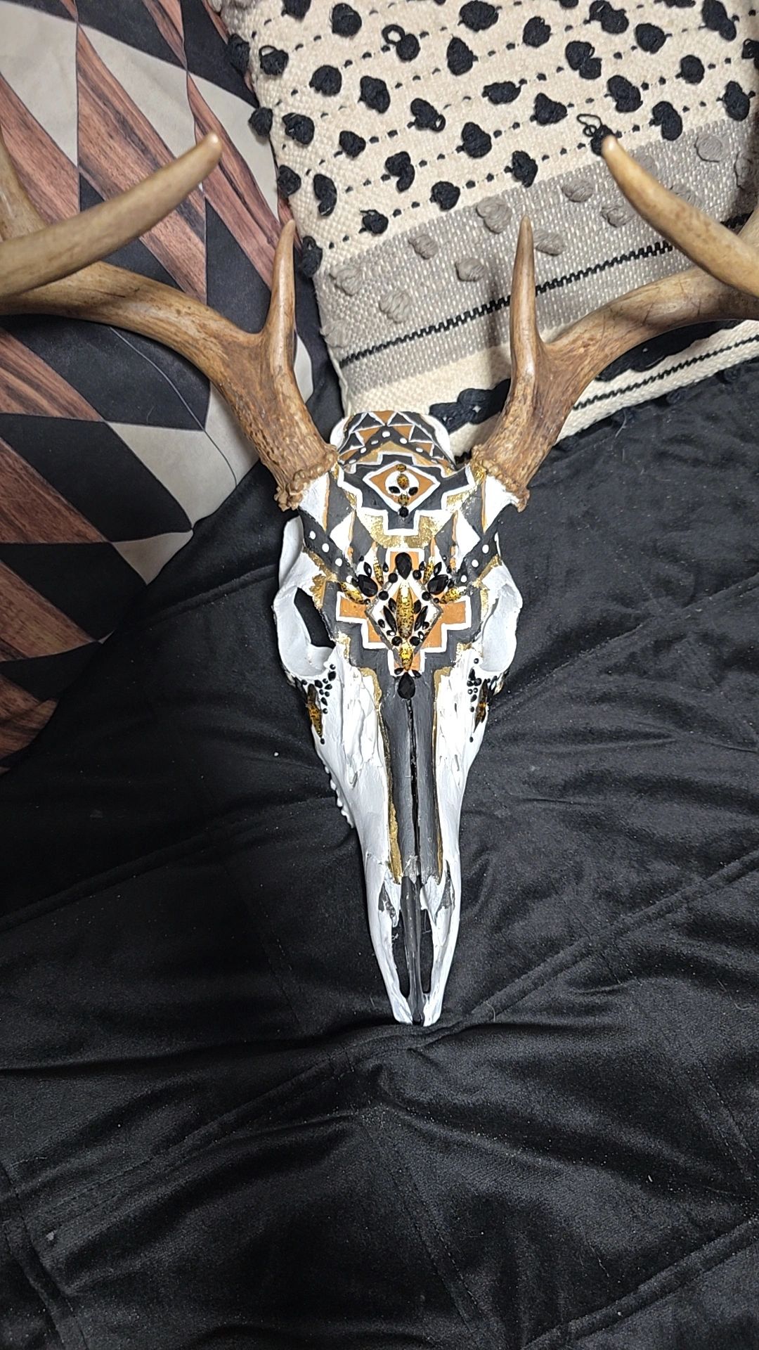 Decorated deer skull with geometric patterns and gemstones on fabric.