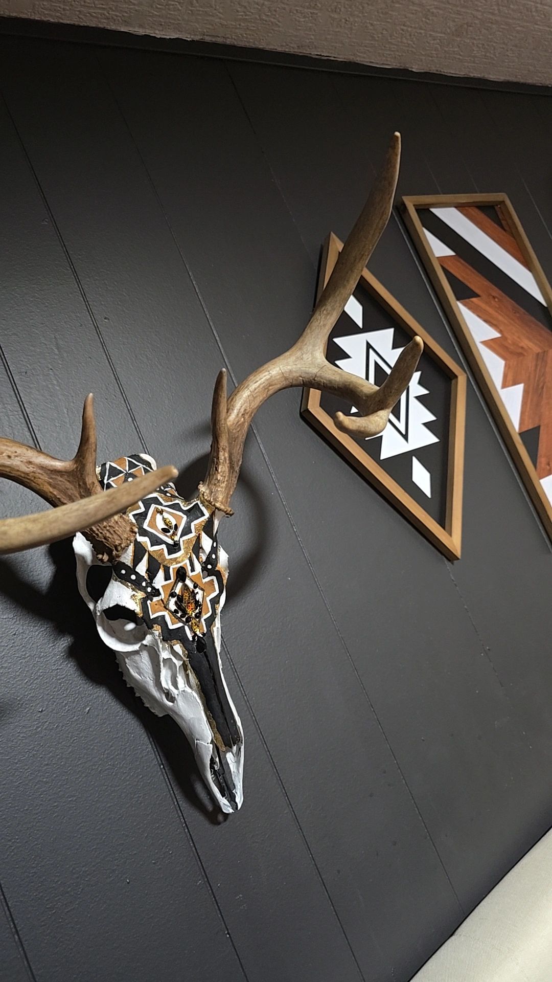 Decorative deer skull with antlers and geometric art on a dark wall.