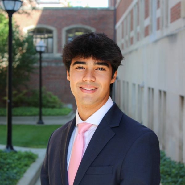 Young man in a suit with a pink tie smiling outdoors.